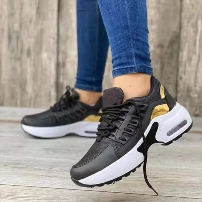 Women's sneakers in black with gold accents, white sole, worn with blue jeans. Fashionable sneakers, ideal for leisure and sport.