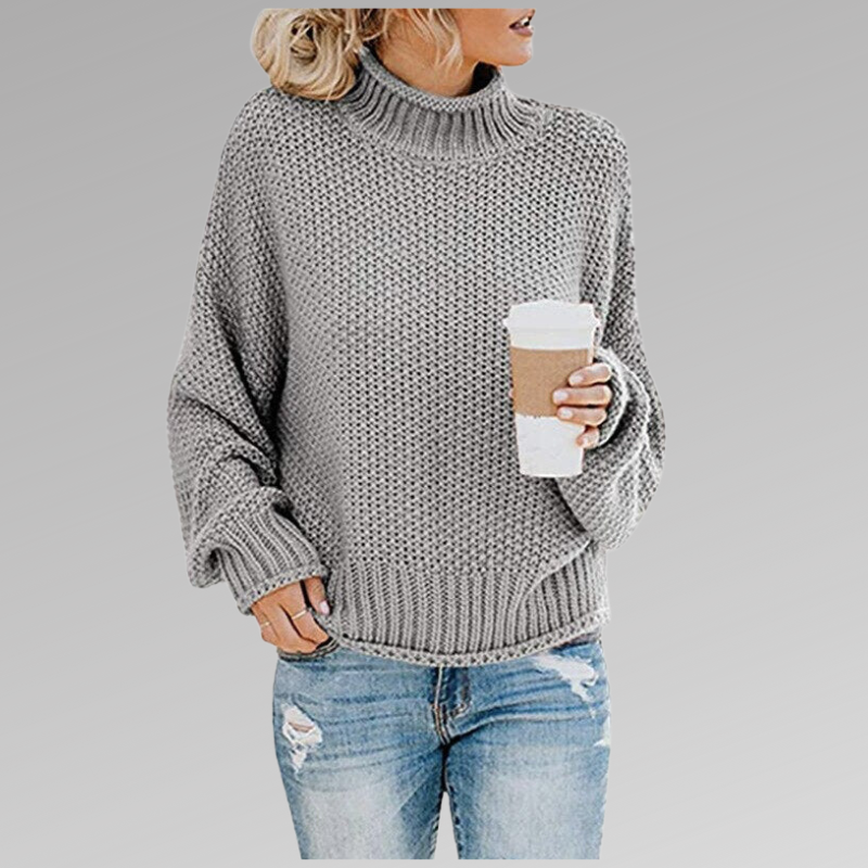 Woman in a gray knit sweater holding a coffee cup, wearing ripped jeans. Fashion trend, fall fashion, casual style, cozy look.