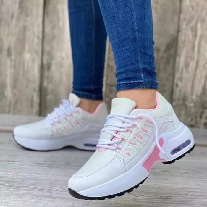 White women's sneakers with pink accents, worn by a person in blue jeans. Fashionable sneakers, ideal for leisure and sport.