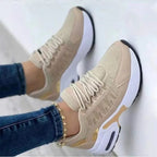 Beige sneakers with white sole, gold accents and laces, worn by a person in blue jeans. Fashionable women's sneakers.