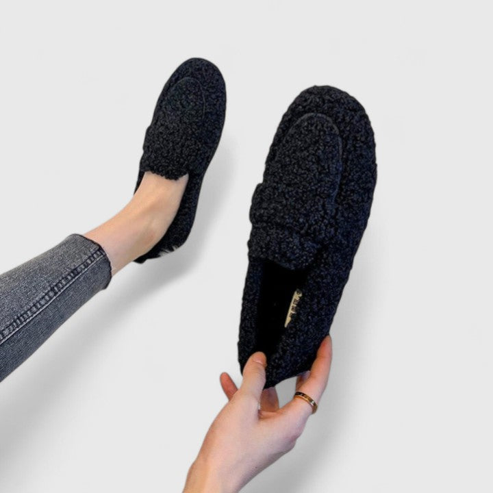 Black, fluffy slippers on feet, worn by a person in jeans. Comfortable, warm slippers for women. Ideal for cozy winter evenings.