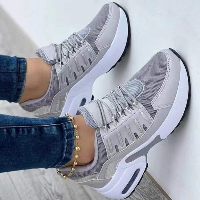 Gray women's sneakers with white sole, mesh upper and laces, worn with blue jeans and a gold anklet.